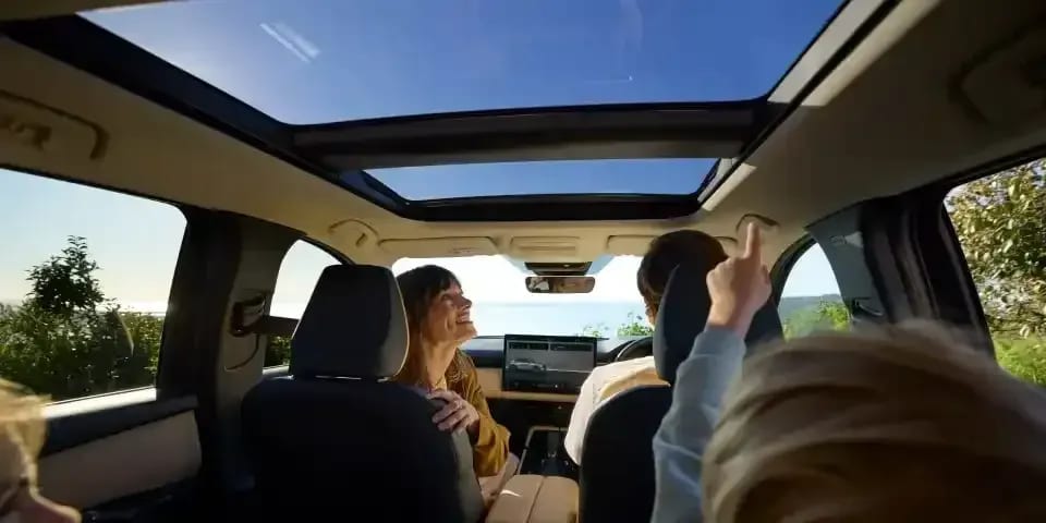 Interior view from back to front of the Mazda CX-5 SUV with a man and woman sitting in the front and a child sitting in the rear looking up through the panoramic glass sunroof