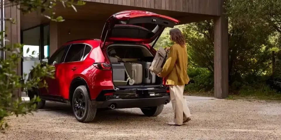 Woman loading luggage into the open boot of a Soul Red Mazda CX-5 SUV parked in a driveway