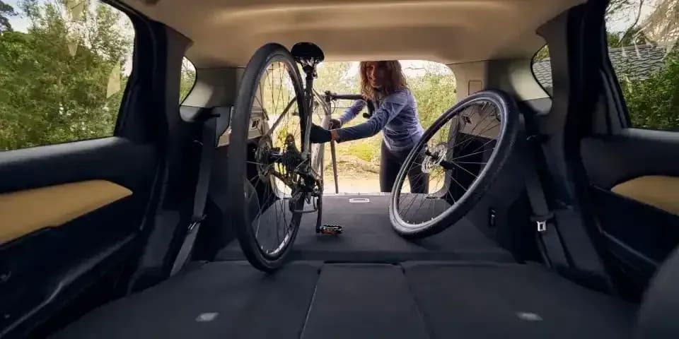 Looking back through the folded seats and the open tailgate of a Mazda CX-5 SUV with a woman loading a mountain bike into the back of the car