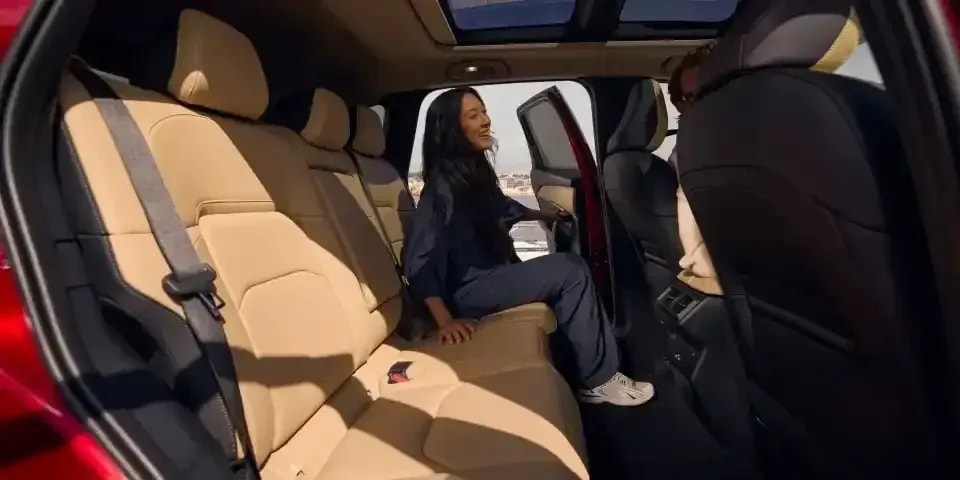 Looking across the tan leather rear seat bench of the Mazda CX-5 SUV with a woman sitting in the outer rear seat with the door open