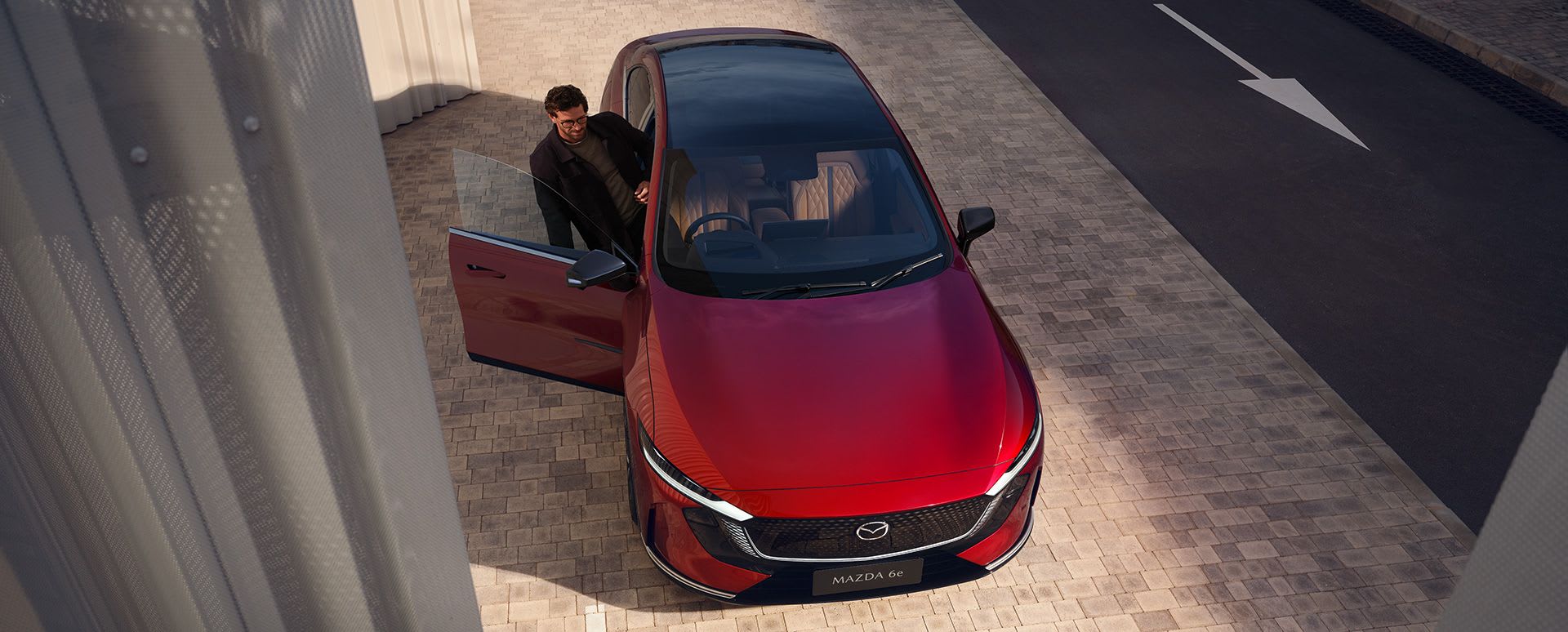 Top down view of a Soul Red all-electric Mazda 6e hatchback with a man getting into the driver's door