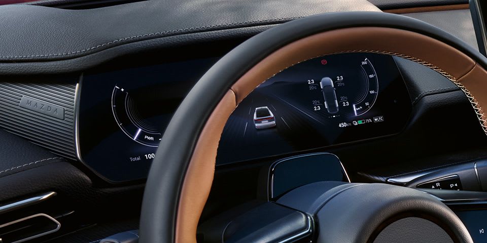 Looking through the top of the steering wheel onto the digital instrument cluster of an all-electric Mazda 6e hatchback