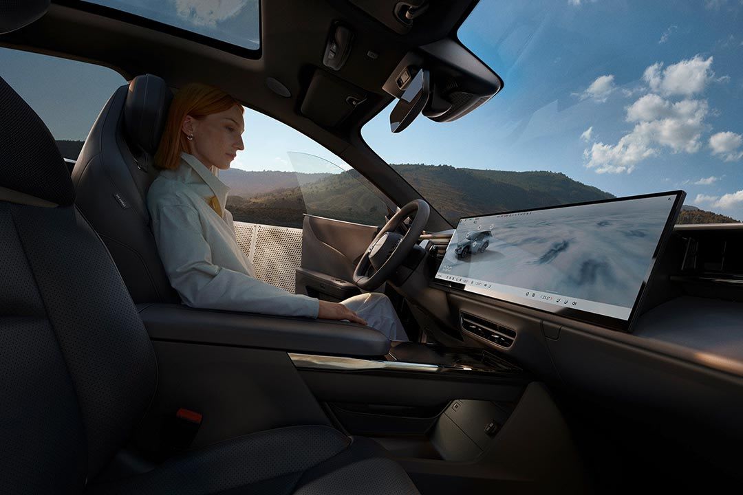 Side view of a woman behind the wheel of an all-electric Mazda CX-6e SUV showing the smart cockpit with large centre touchscreen