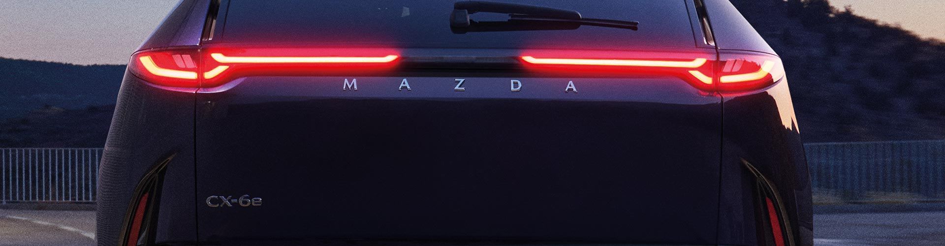 Rear view of an all electric Mazda CX-6e SUV at dusk with the LED rear tail lights on