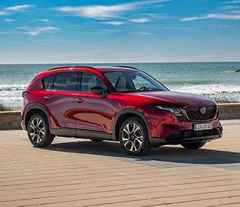 Front three quarter view of a Soul Red all-new Mazda CX-5 SUV parked in a beach carpark