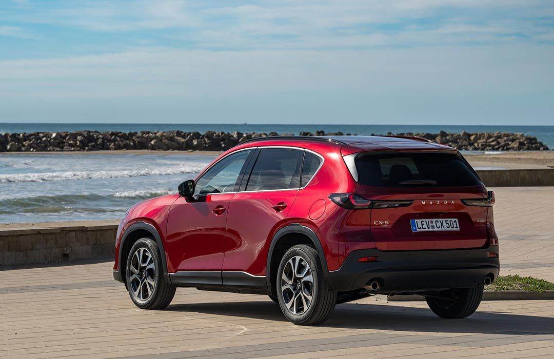 Rear three quarter view of a Soul Red all-new Mazda CX-5 SUV parked at a beach carpark