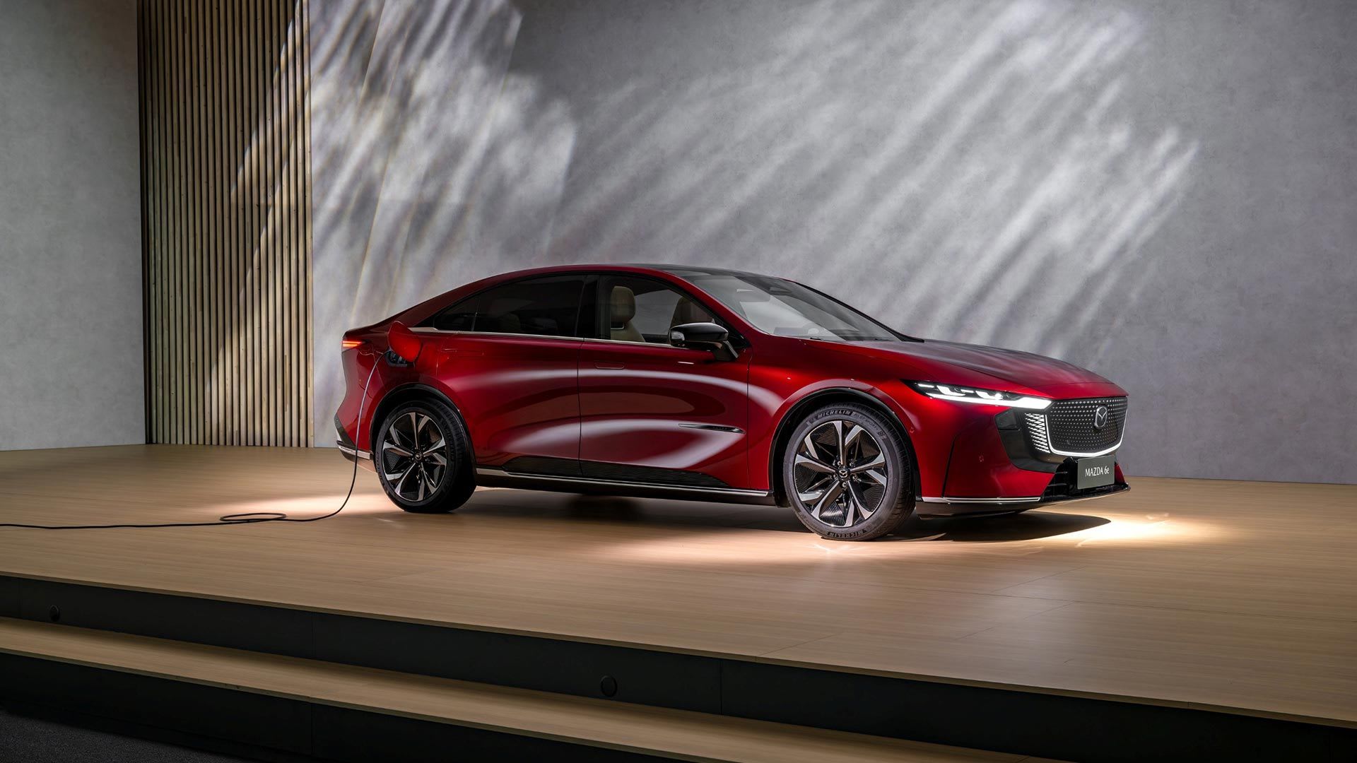 Front three quarter view of a red all-new, all-electric Mazda 6e on display and plugged in