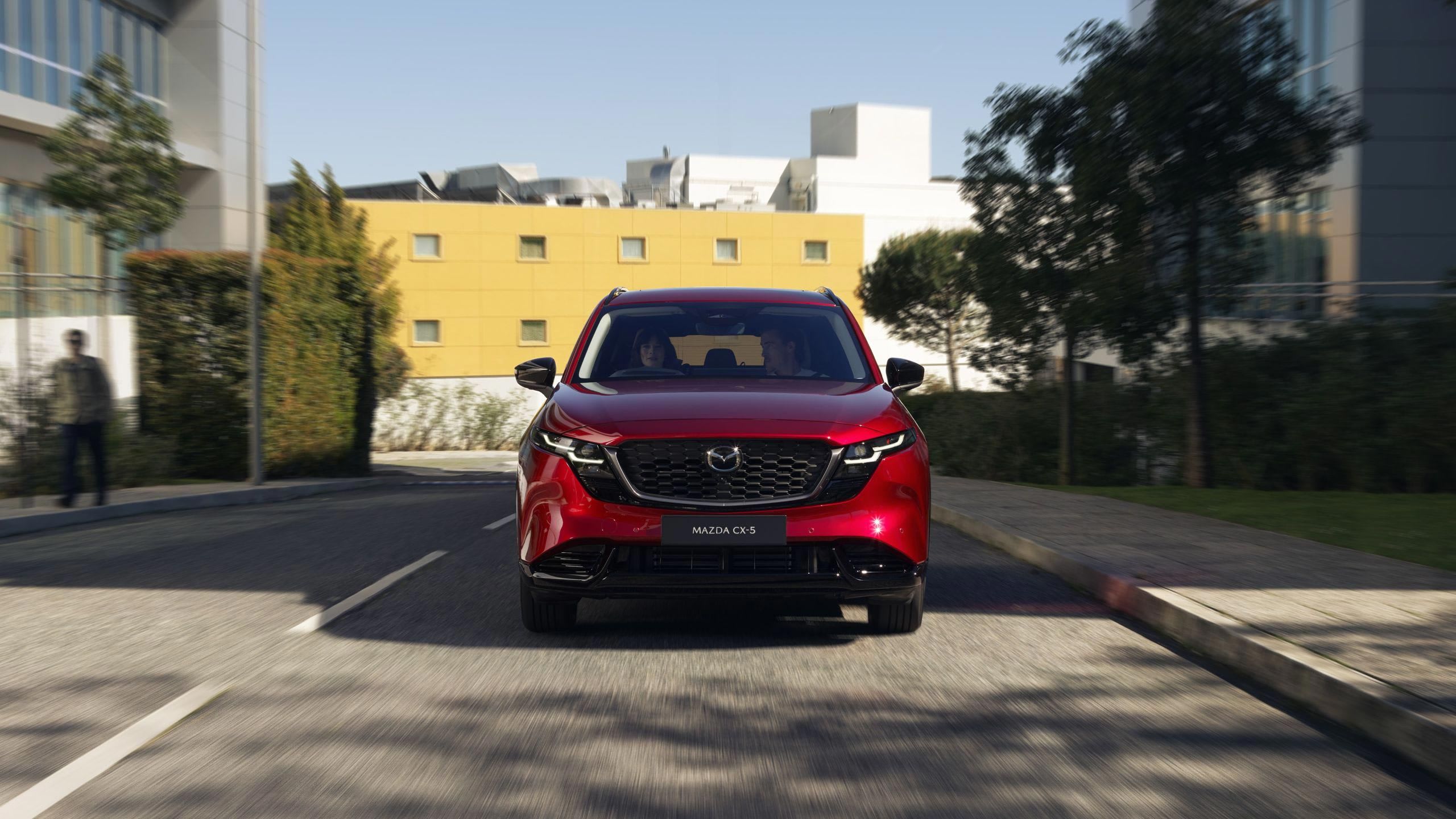 Front view of a Soul Red all-new Mazda CX-5 SUV in a carpark in front of a yellow apartment building
