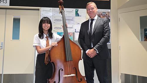 Student from Massey High School holding a double bass standing next to a teacher