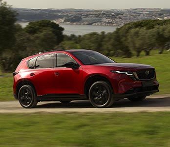 Side view of a Soul Red all-new Mazda CX-5 SUV driving on an open road