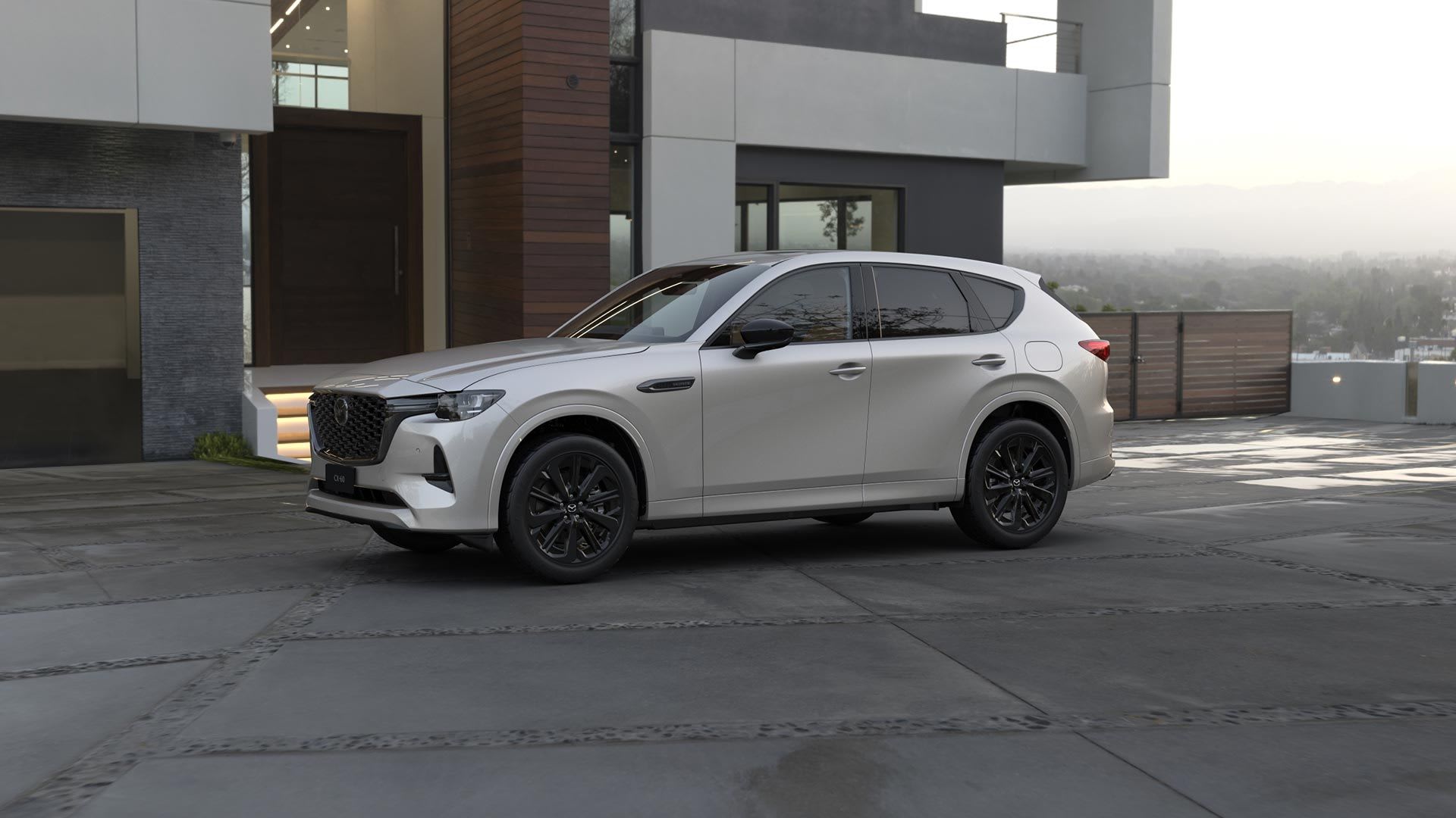 Front three quarter view of a Rhodium White Mazda CX-60 SUV hybrid parked in front of a designer home
