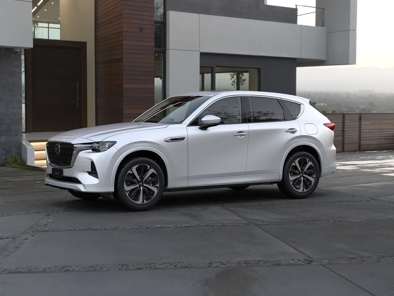 Front three quarter view of a Rhodium White Mazda CX-60 Takami Hybrid SUV parked in front of a designer house