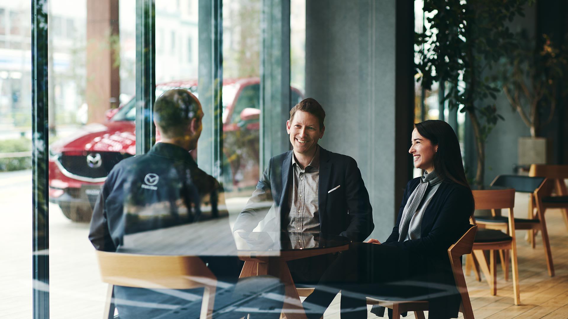 Mazda dealer staff member talking to man and woman customers at a desk inside a Mazda dealership