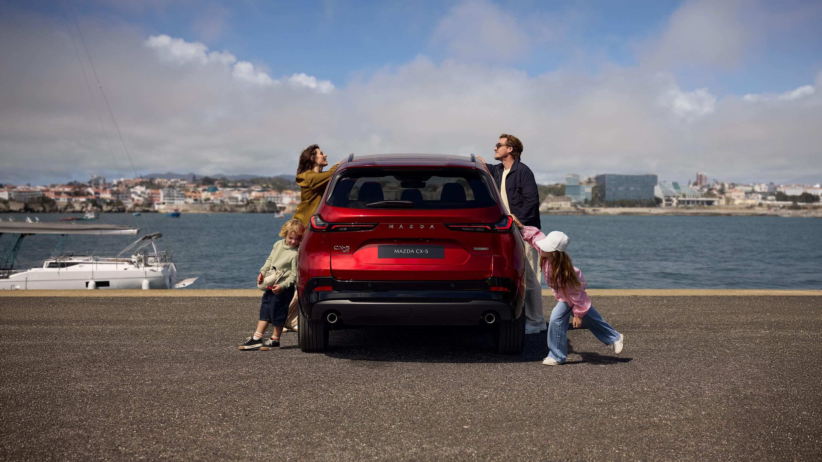 Rear view of a Soul Red Mazda CX-5 SUV at the harbour with a young family standing next to the car