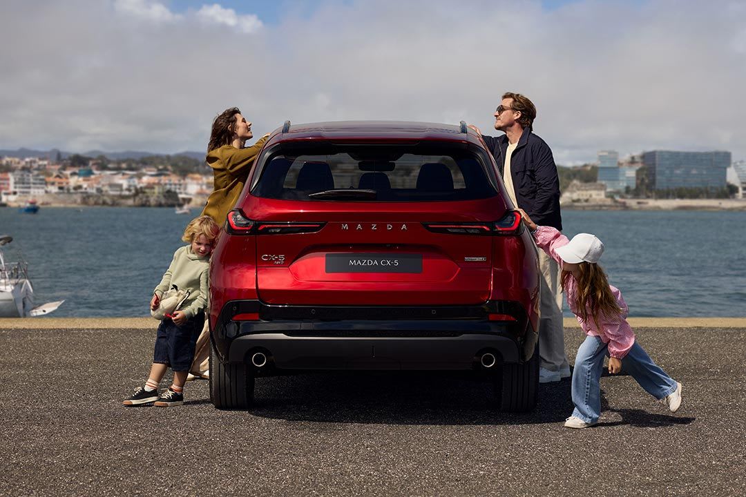 Rear view of a Soul Red Mazda CX-5 SUV at the harbour with a young family standing next to the car