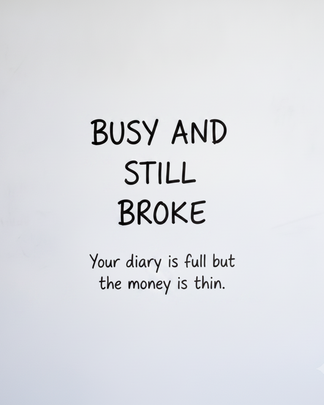 Whiteboard with the words Busy and still broke written in black marker with a smaller line underneath about a full diary and thin money