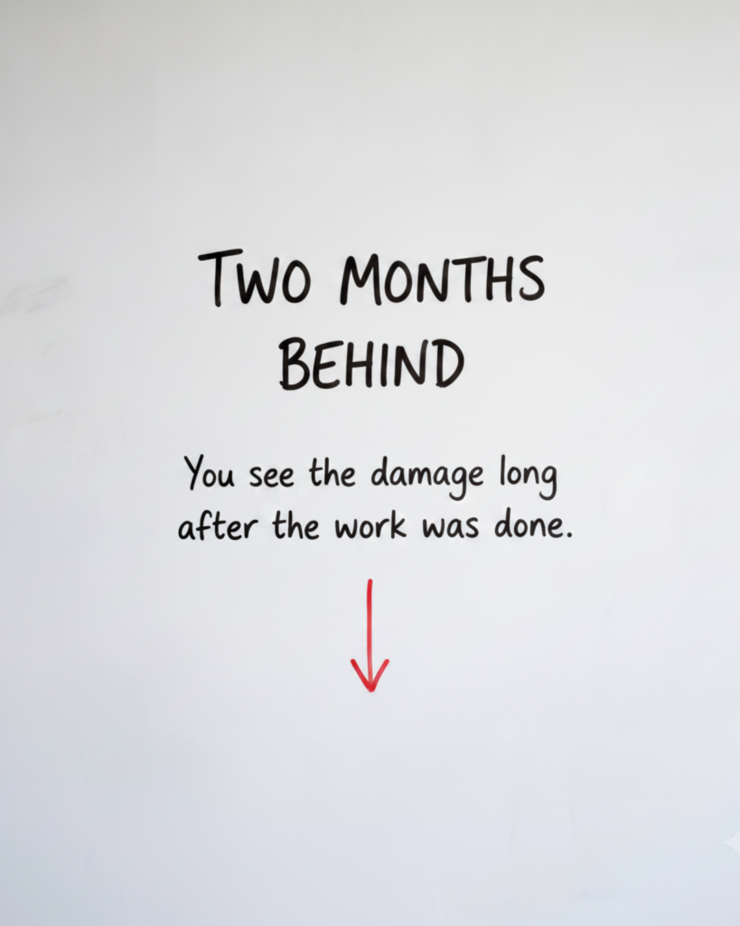 Whiteboard with the words TWO MONTHS BEHIND written in black marker above a red downward arrow