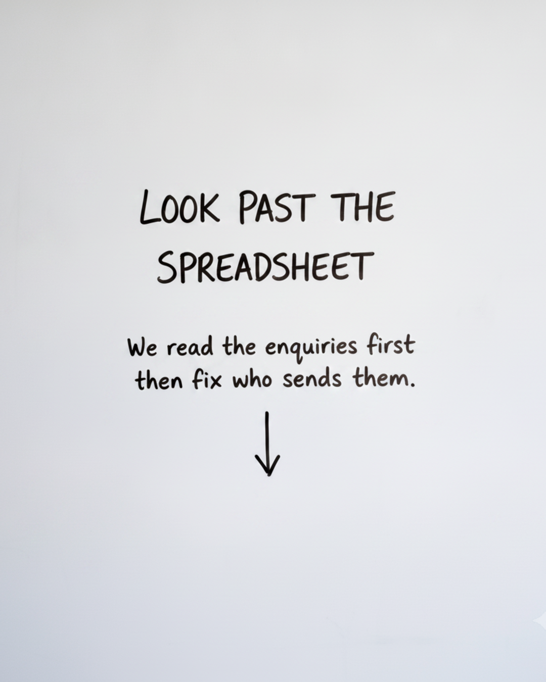 Whiteboard with the words LOOK PAST THE SPREADSHEET written in black marker above a downward arrow