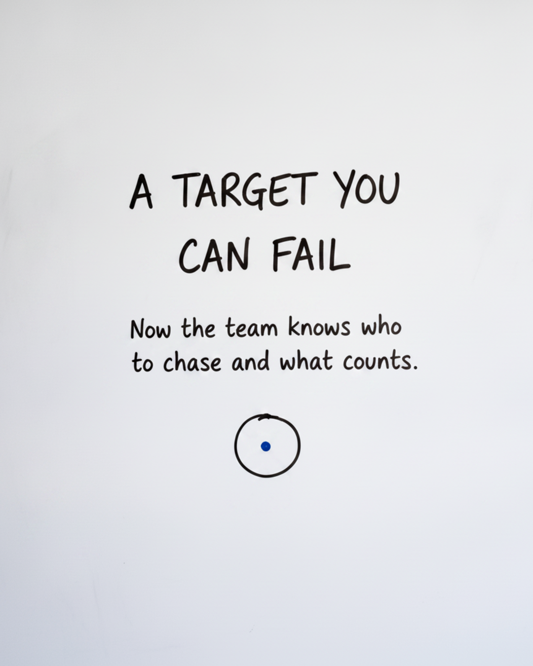 Whiteboard with the words A target you can fail written in black marker above a circle with a small blue dot in the middle