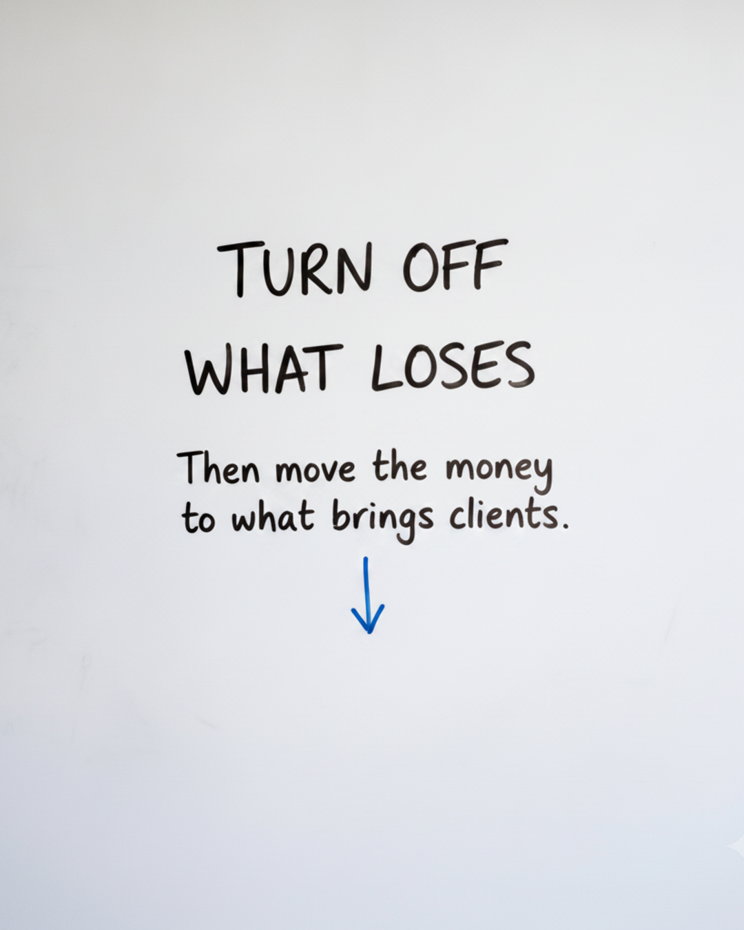 Whiteboard with the words Turn off what loses written in black marker, above a short downward arrow drawn in blue