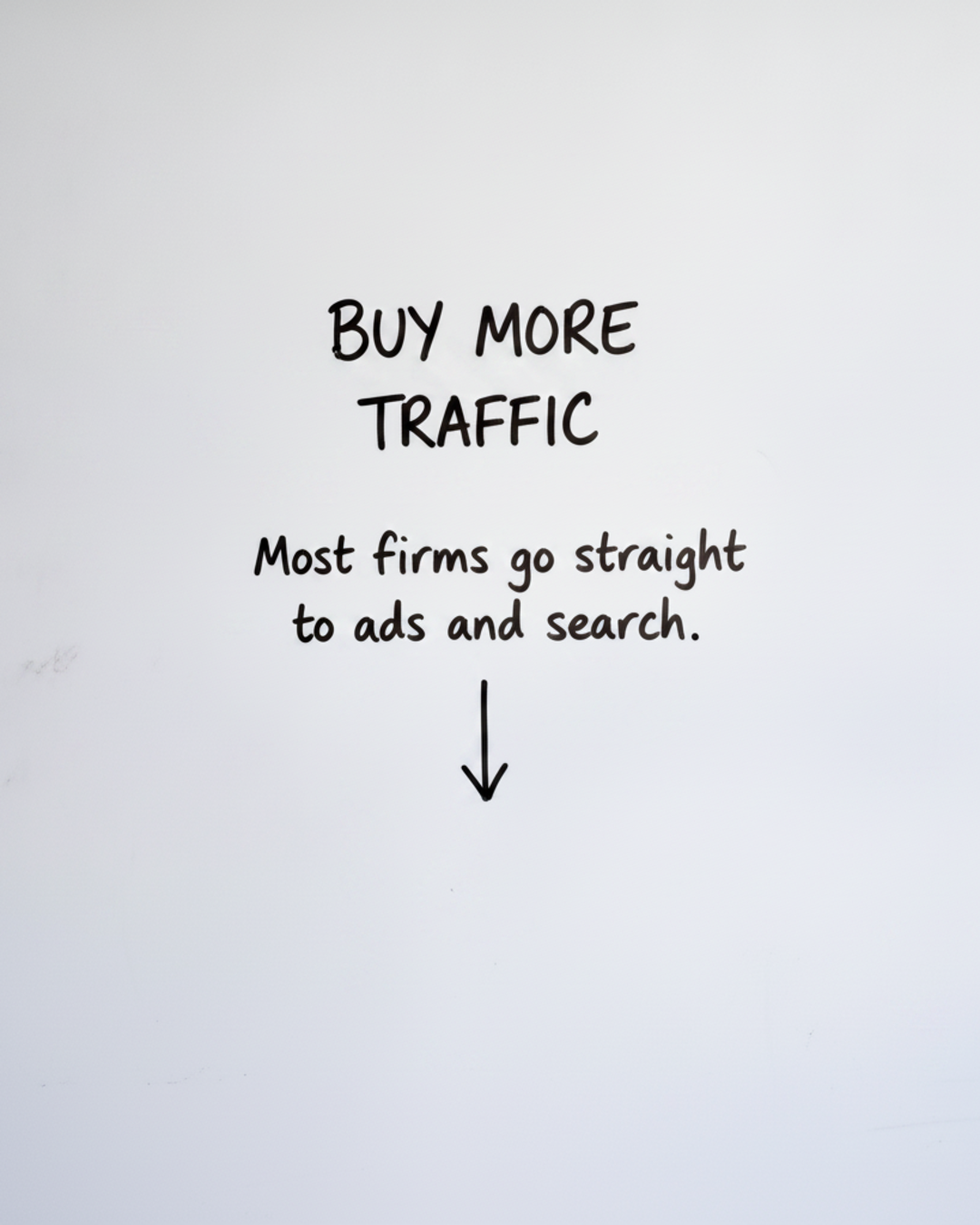 Whiteboard with the words Buy more traffic in black marker above a downward arrow