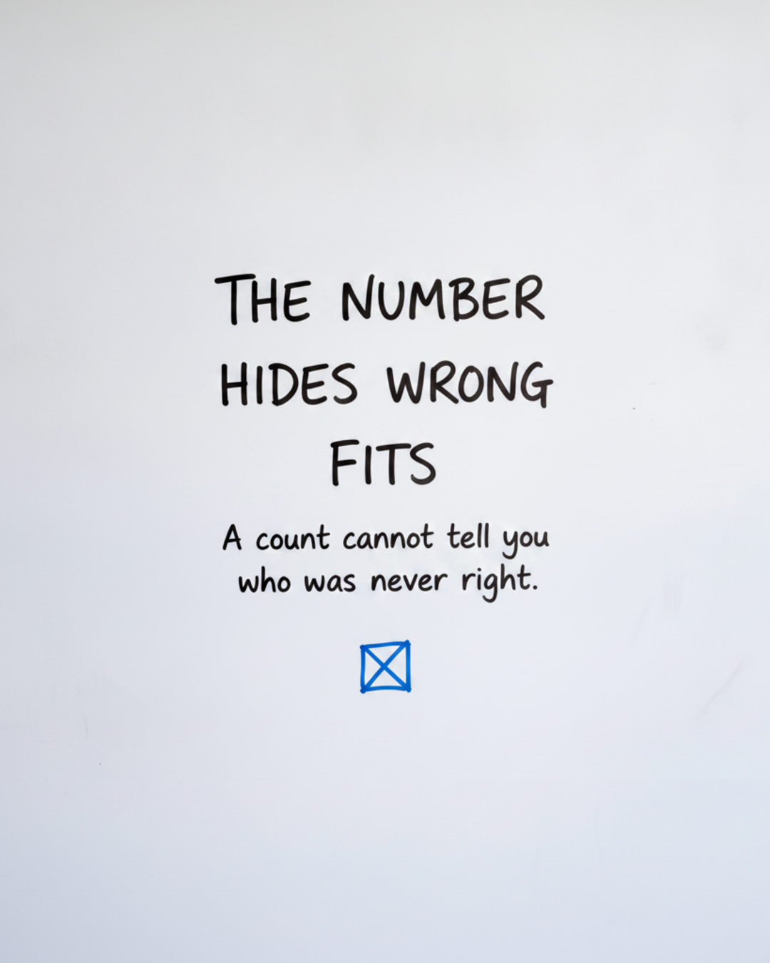 Whiteboard with the words THE NUMBER HIDES WRONG FITS written in black marker above a small box crossed out in blue