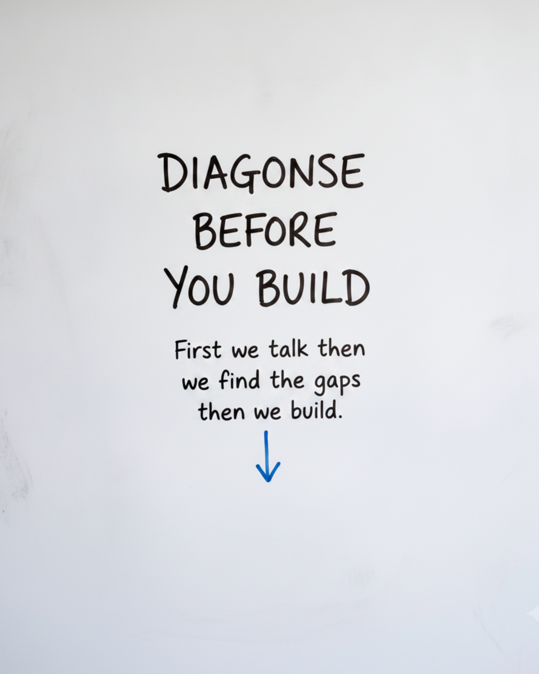 Whiteboard with the words DIAGNOSE BEFORE YOU BUILD in black marker above a blue downward arrow