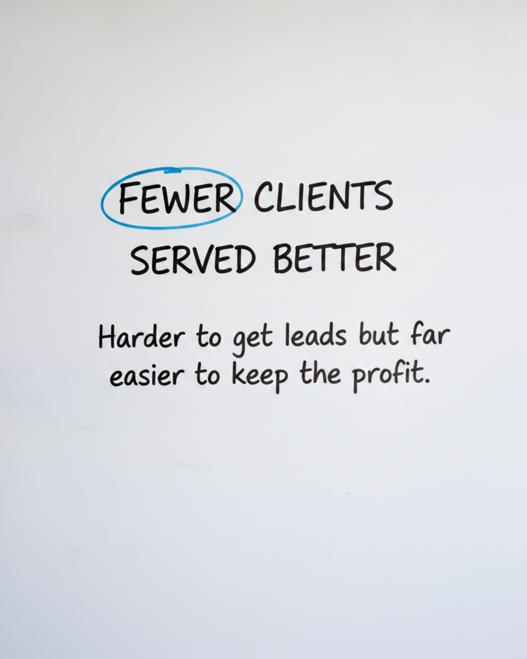 Whiteboard with the words FEWER CLIENTS SERVED BETTER in black marker, with the word FEWER circled in blue