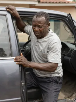 Nigerian man bracing on his car door to stand up
