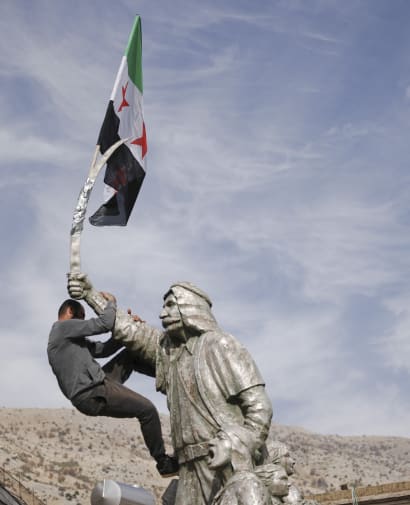 En mand placerer et flag i toppen af en statue i det sydlige Syrien.