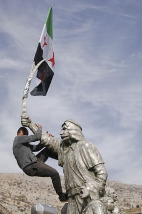 En mand placerer et flag i toppen af en statue i det sydlige Syrien.