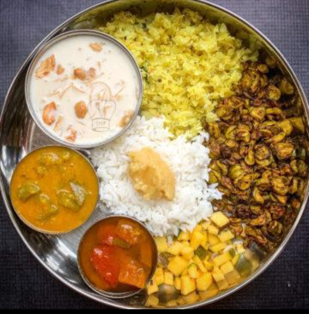 A festive Tamil Brahmin meal: rice with ghee, sambar, rasam, vegetable curry, lemon rice, raw mango pieces and payasam.
