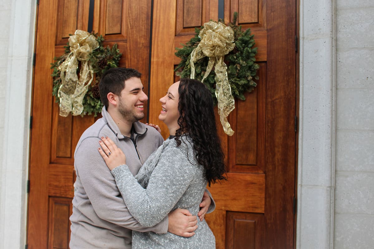A couple in front of doors with holiday wreaths