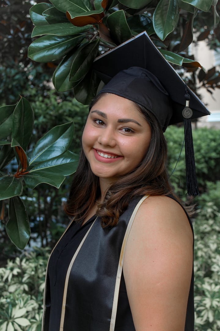 Girl graduating from UCF with greenery in the background musn56