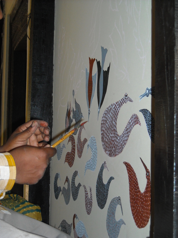 Artist hand-painting a Gond tribal mural — the characteristic dot-and-line style used to depict animals and trees