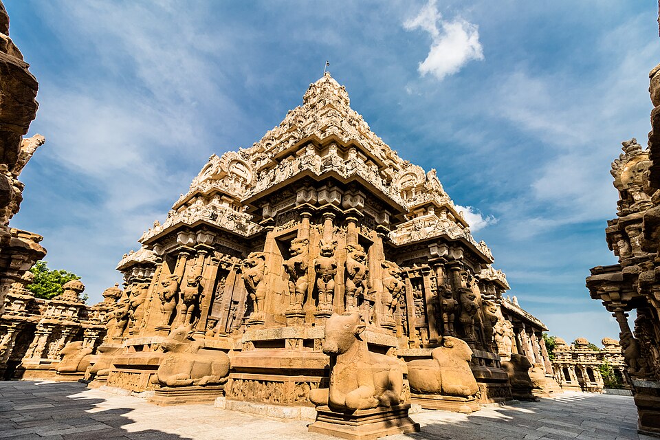 The pyramidal sandstone vimana of the Kailasanathar temple at Kanchipuram, with seated Nandi bulls and carved lion pillars in front and the cell-lined enclosure wall on either side