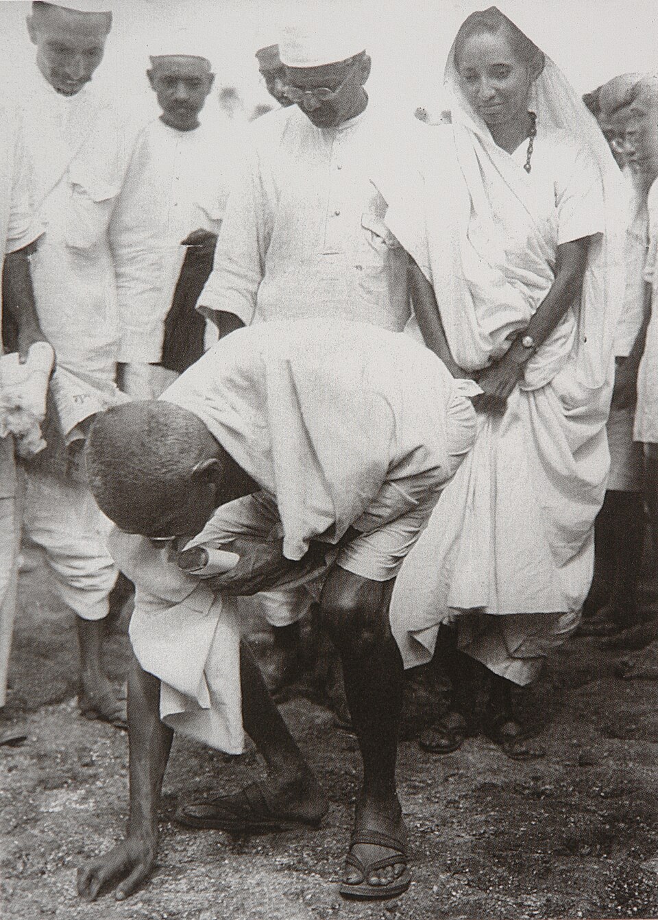 Mahatma Gandhi bending down to pick up a handful of salt from the shore at Dandi while khadi-clad companions watch