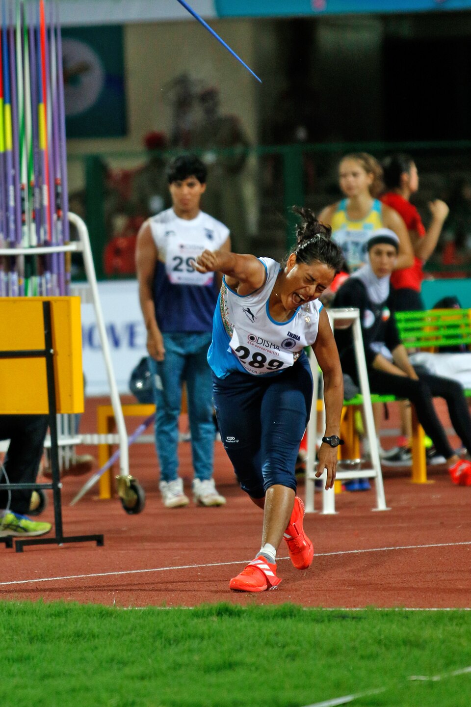 Indian javelin thrower Annu Rani in the follow-through of a throw, the javelin still airborne above her, at a stadium athletics final