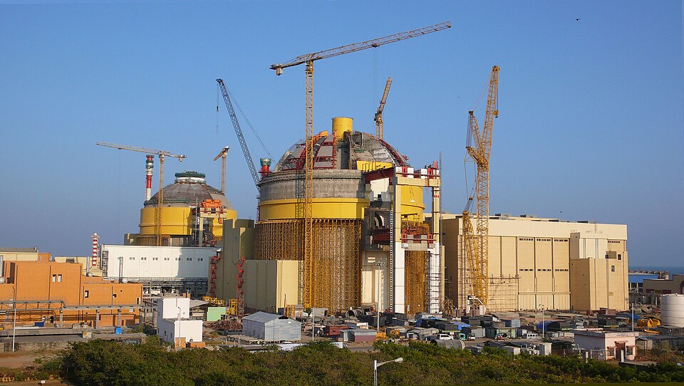 The two VVER reactor containment domes of the Kudankulam nuclear power plant, ringed by construction cranes and turbine halls near the coast