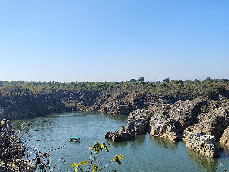 The Narmada river winding between the pale marble cliffs of the gorge at Bhedaghat, with a small tourist boat on the green water