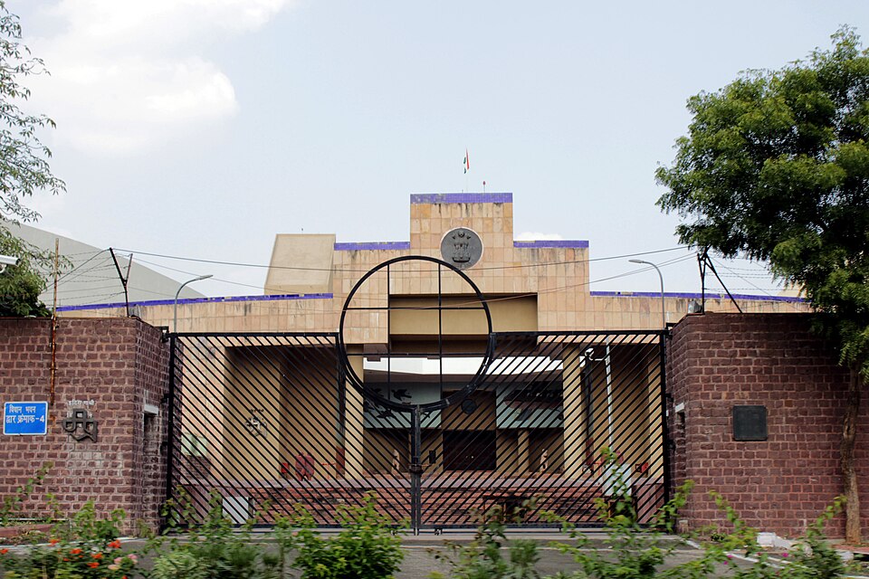 The gated entrance of the Madhya Pradesh Vidhan Bhavan in Bhopal, with the state emblem set on the sandstone facade above the doorway