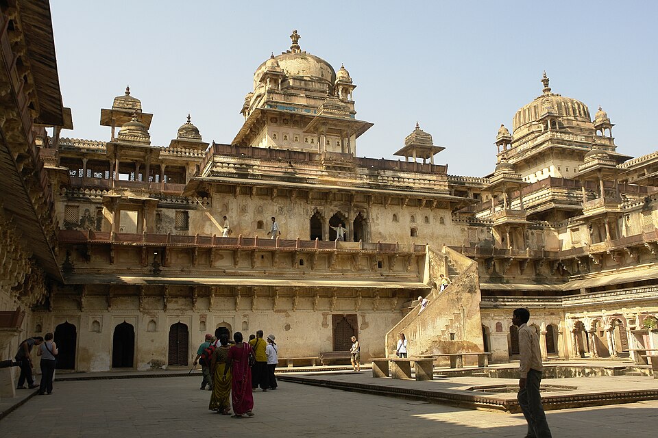 The inner courtyard of Jahangir Mahal at Orchha, ringed by tiered balconies and domed pavilions with visitors crossing the paved court