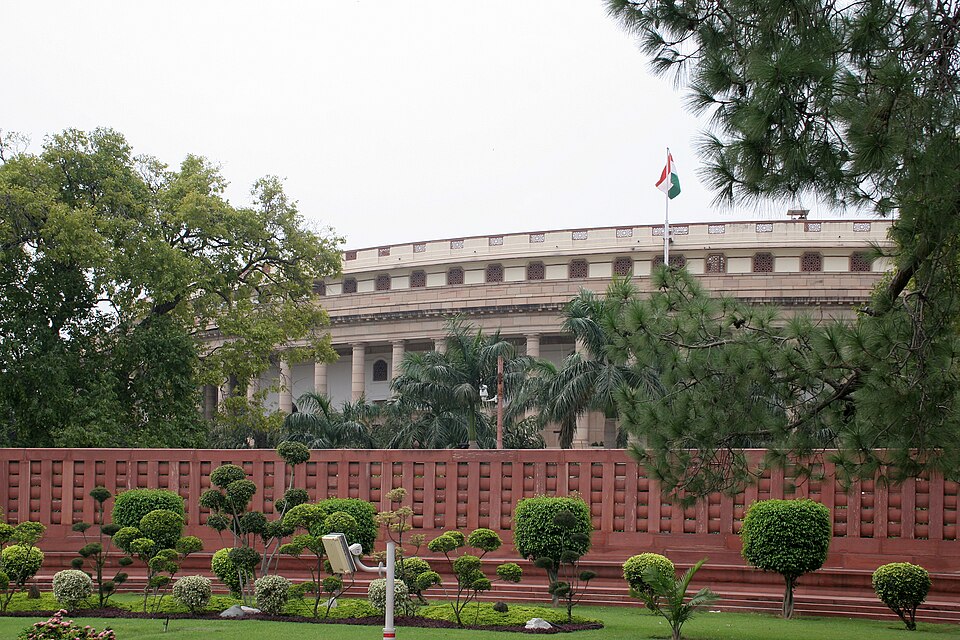 The circular colonnaded old Parliament House in New Delhi seen over its red sandstone boundary wall, the national flag flying above it