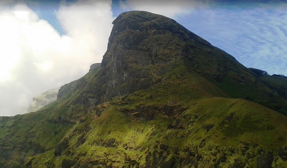 The horse-face-shaped summit of Kudremukh rising above grassy Western Ghats slopes with cloud drifting past its flank