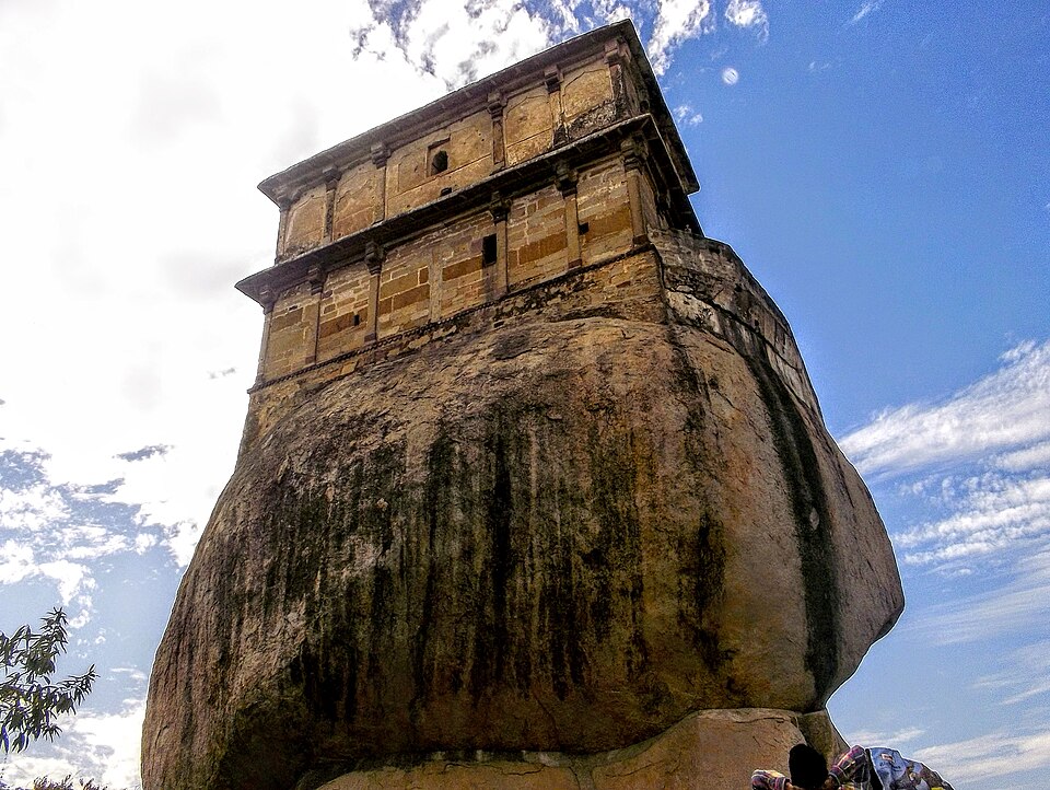 The stone Madan Mahal fort perched on a rounded granite boulder at Jabalpur, seen from below against a blue sky
