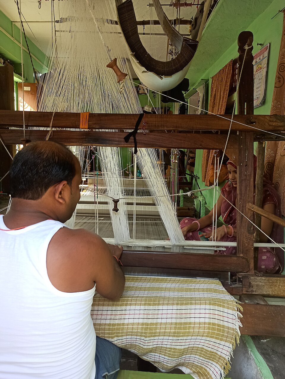 A weaver at a wooden pit loom in Chanderi working on a striped handloom saree, the warp threads stretched above the frame