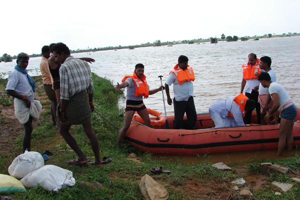 NDRF personnel in orange life jackets with an inflatable rescue boat helping villagers along a flooded riverbank