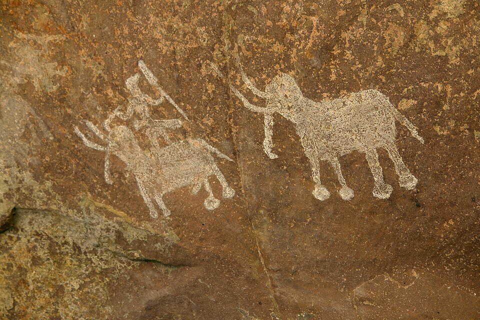 Prehistoric white rock paintings at Bhimbetka showing an elephant and a rider figure on the ochre cave wall
