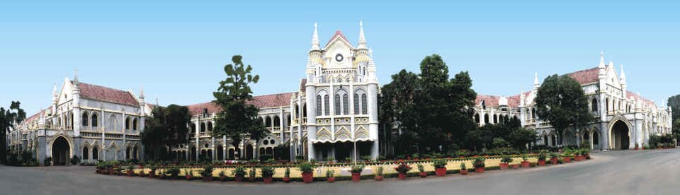 Panoramic view of the white Gothic-revival Madhya Pradesh High Court building at Jabalpur, with its central gabled porch, arcaded wings and a line of potted plants along the drive