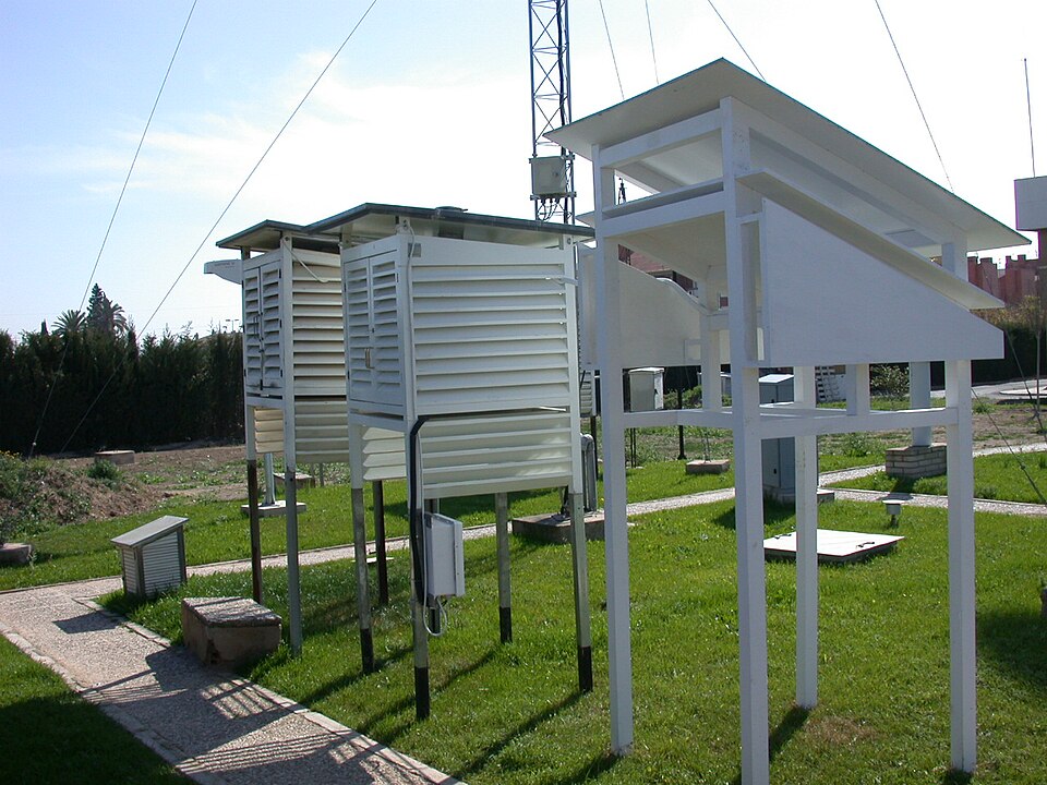 White louvred thermometer screens raised on legs in the grassed enclosure of a meteorological observatory, with a mast behind them